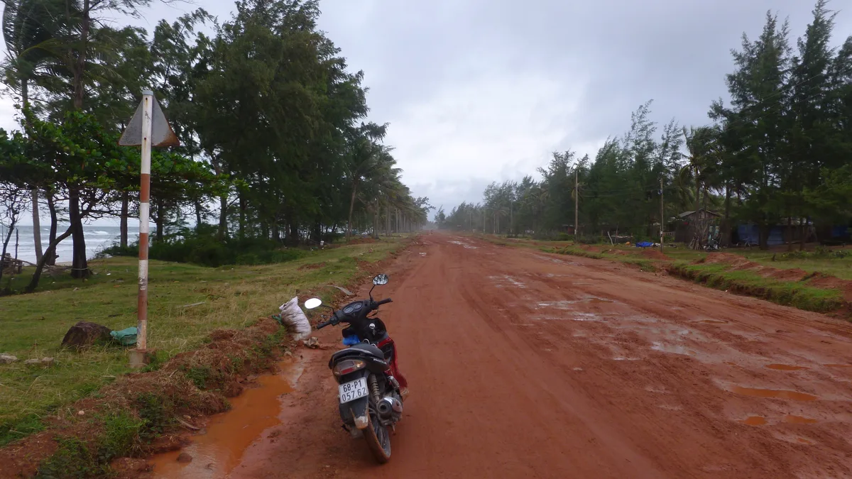 Motorbike parked beside a muddy rural road under an overcast Vietnam sky