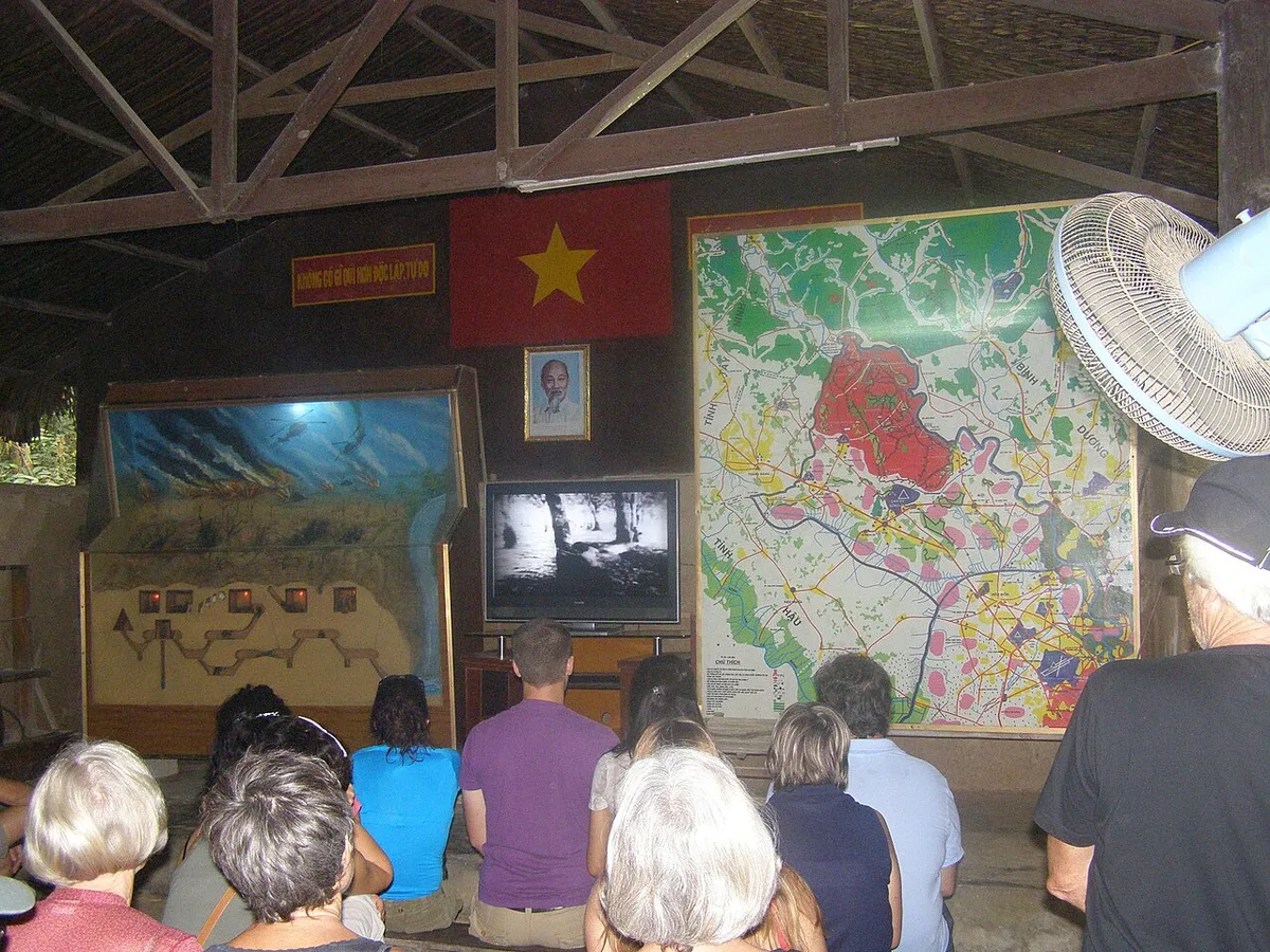 Turistoj spektas dokumentan filmon en ekspoziciejo en la Củ Chi tuneloj, illustrating Step-by-Step Guide to Booking &
