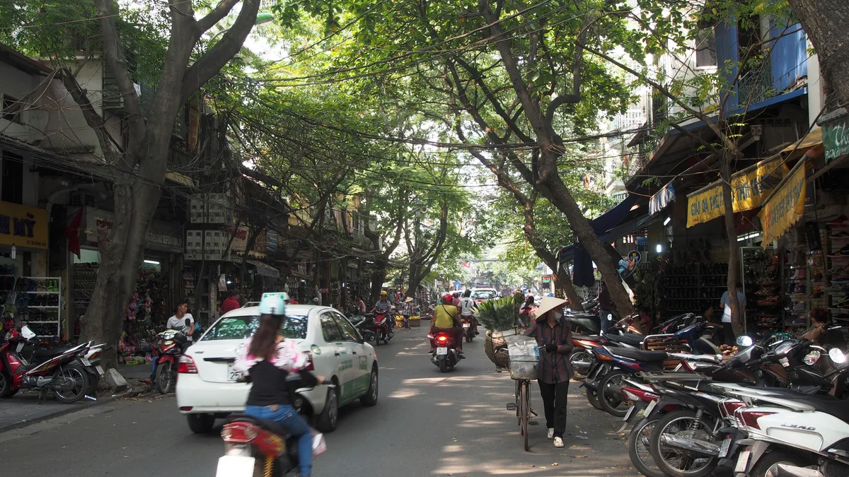Motorbikes and taxis moving through a busy central Hanoi street during the day