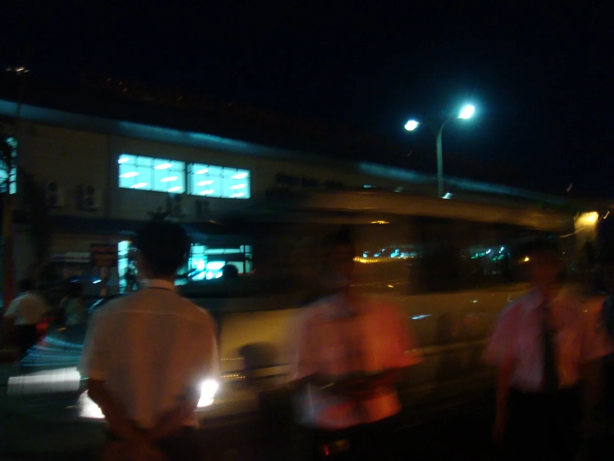 Passengers and a shuttle vehicle outside Phu Bai Airport terminal near Hue at night