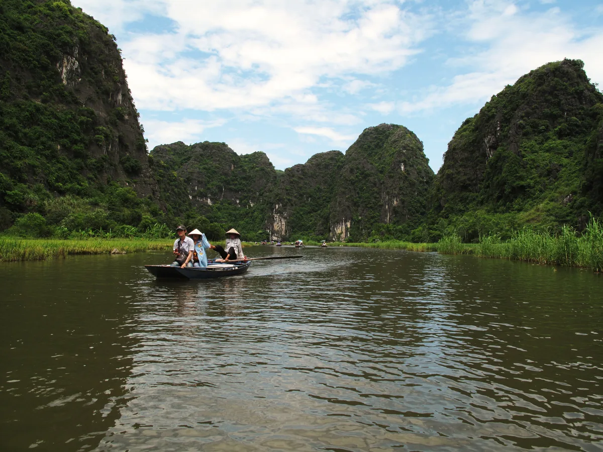 Rowboat crossing calm water beneath limestone karsts and green banks in Ninh Binh