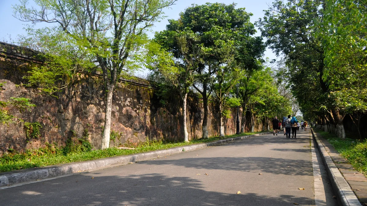 Tree-lined walking route beside the weathered walls of Hue Imperial City