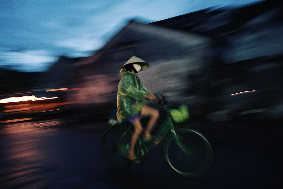 Cyclist wearing a rain poncho on a wet evening street in Hoi An
