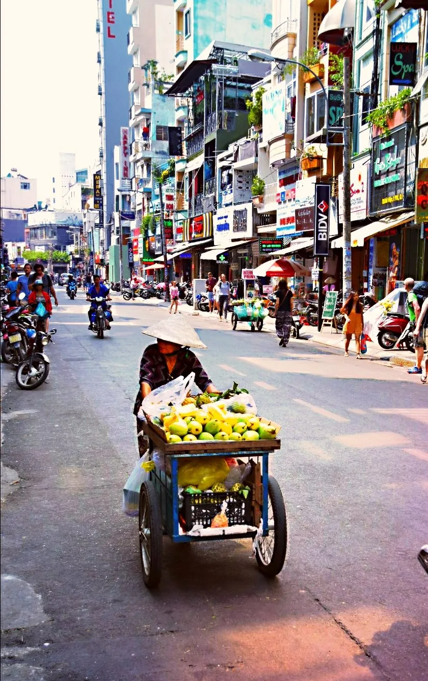 Mobile fruit vendor serving customers on a busy Ho Chi Minh City street